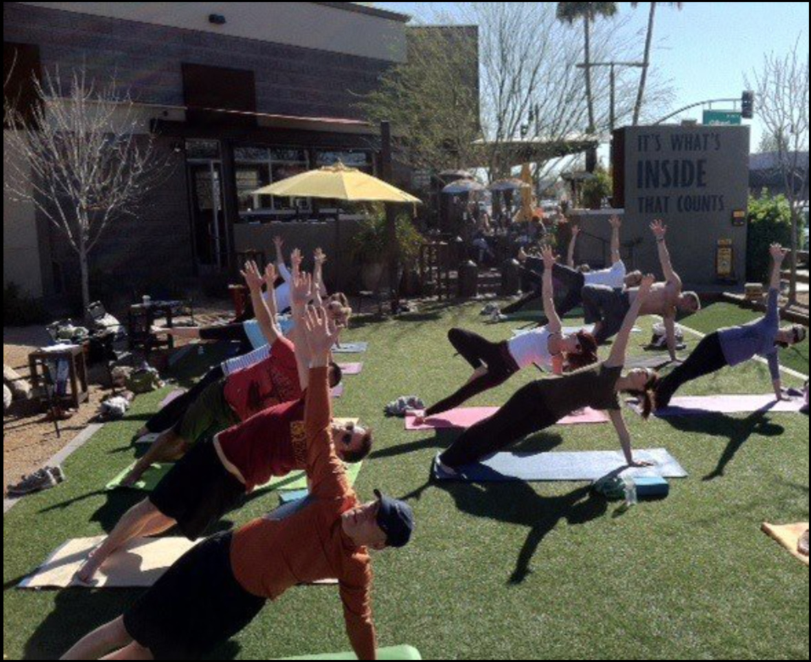 A group practicing yoga poses on the Postino East lawn
