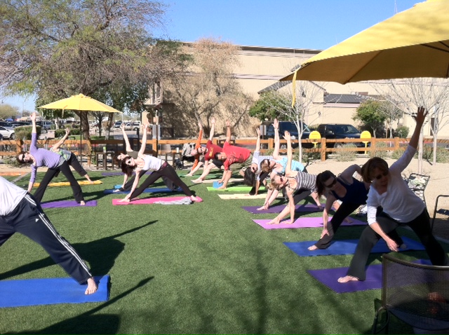 Participants practicing a twisting yoga pose under Postino East umbrellas